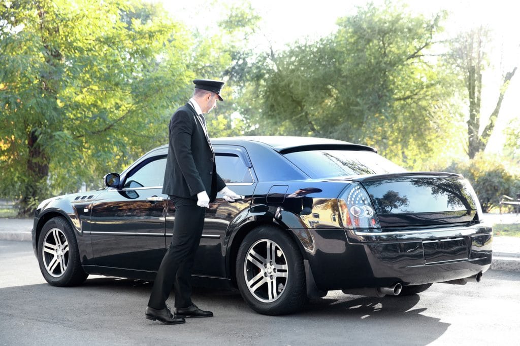 Chauffeur opening back door of black limousine